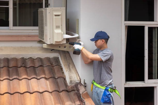 A man repairs an air conditioner, focused on the unit with tools in hand, during AC installation in Glendora and Oakland, CA, in a well-lit indoor environment.